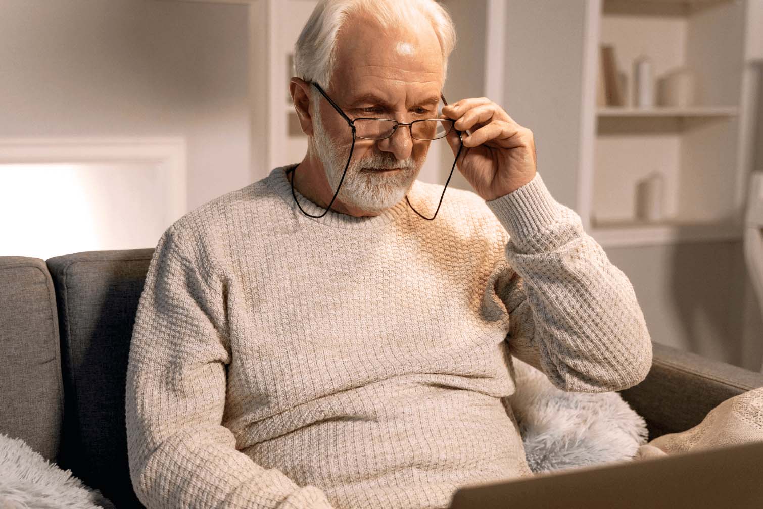 A senior man sitting on a couch, looking at his computer.
