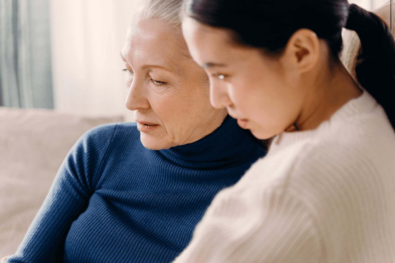 A young girl and a middle-aged woman sitting on a soffa while looking at something together.