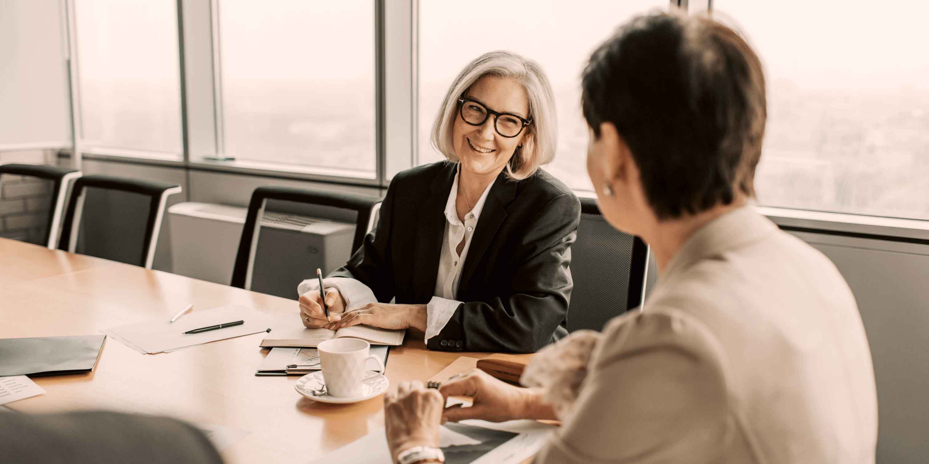 A woman by an office table, smiling towards another person.