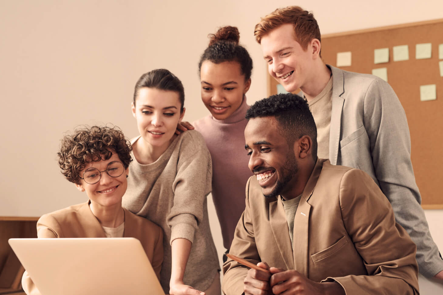 Five people in an office, looking at a laptop screen together.