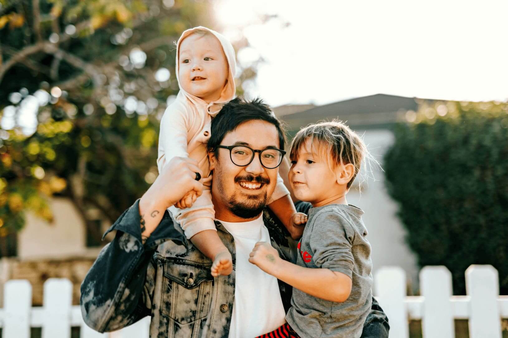 A middle aged man carrying two children in a garden.