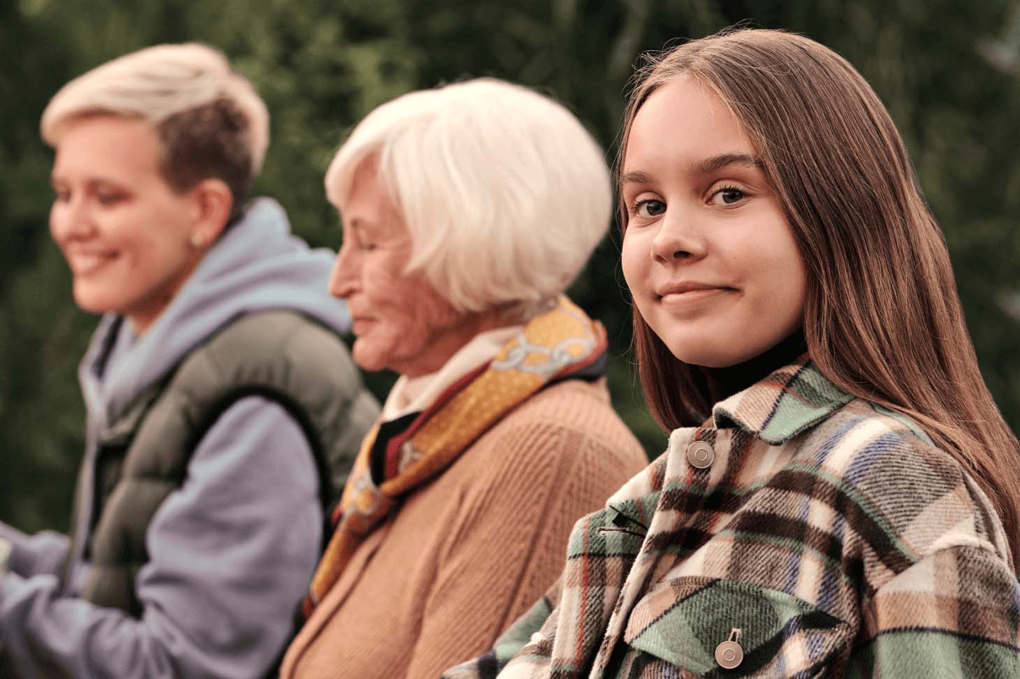 A young girl, accompanied by an elderly woman and a middle-aged woman, looks into the camera while smiling.