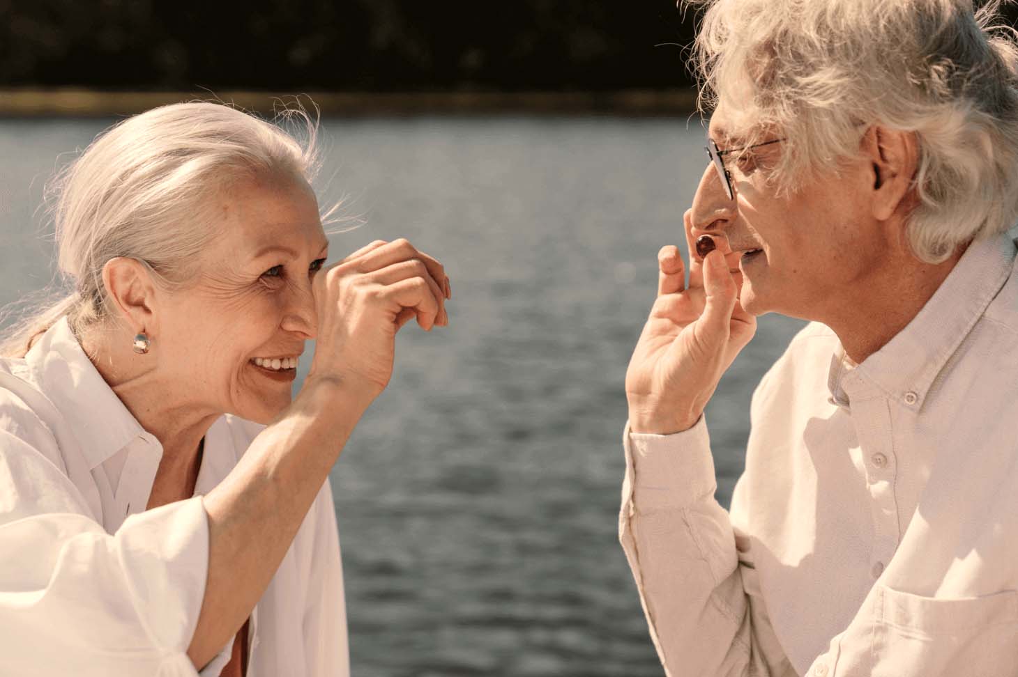 Two elderly people interacting with each other by a lake.