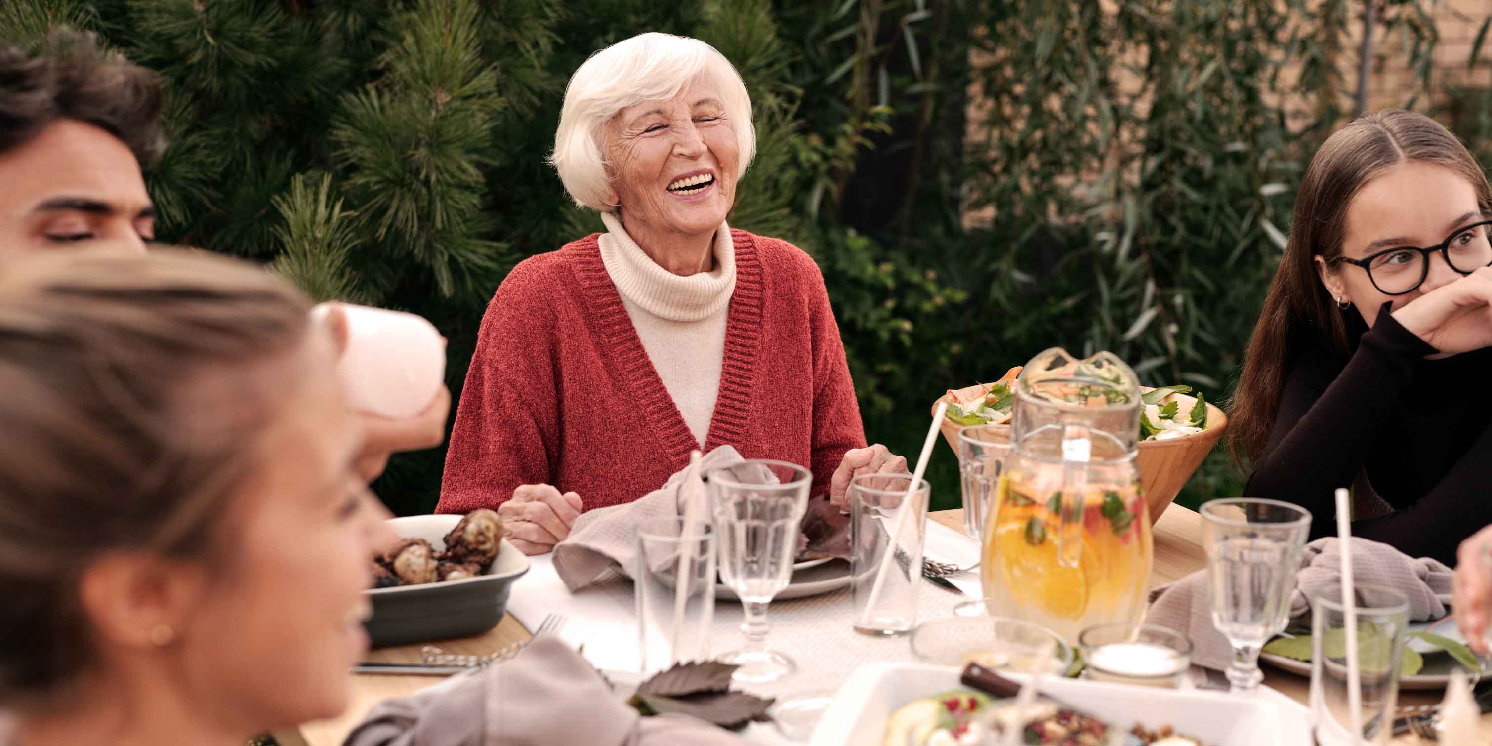 An elderly person at a dinner table laughing together with three younger people.