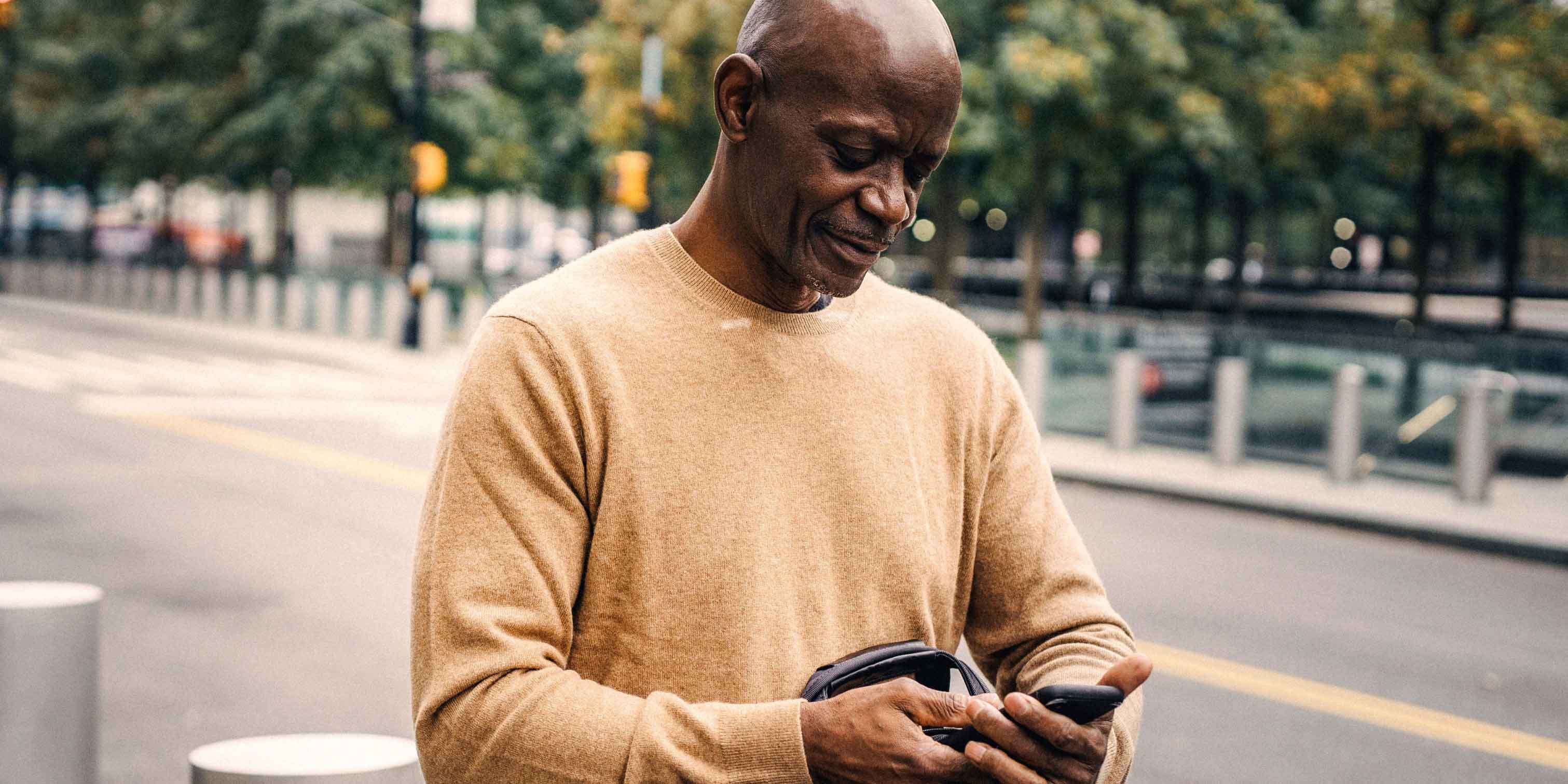 An elderly man walking down a street, holding a smartphone.